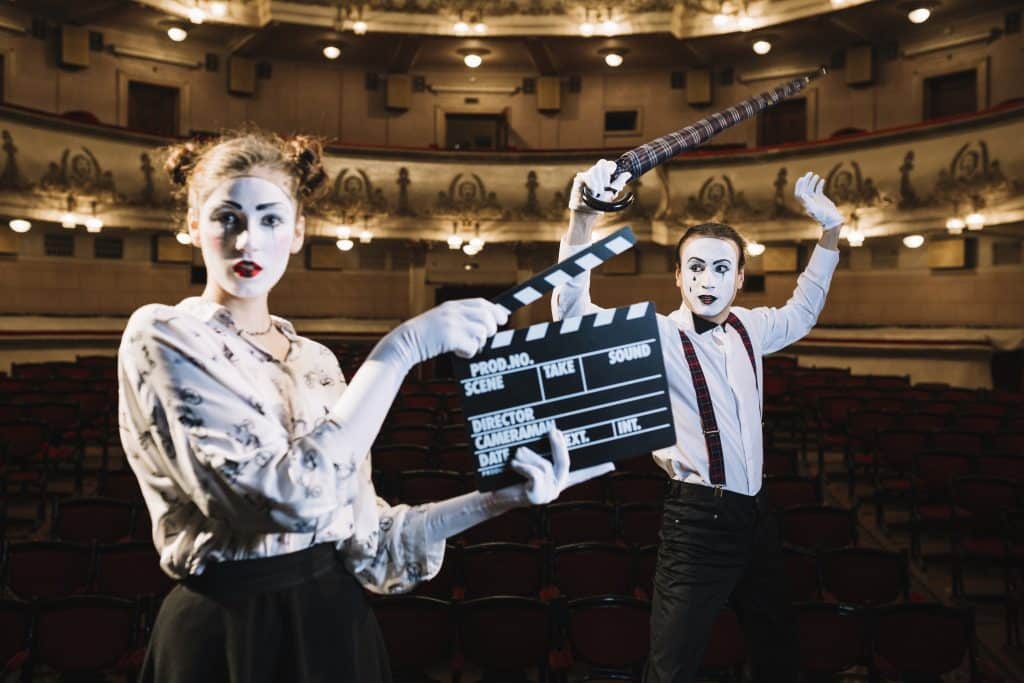 Female mime artist holding clapper front male mime holding umbrella